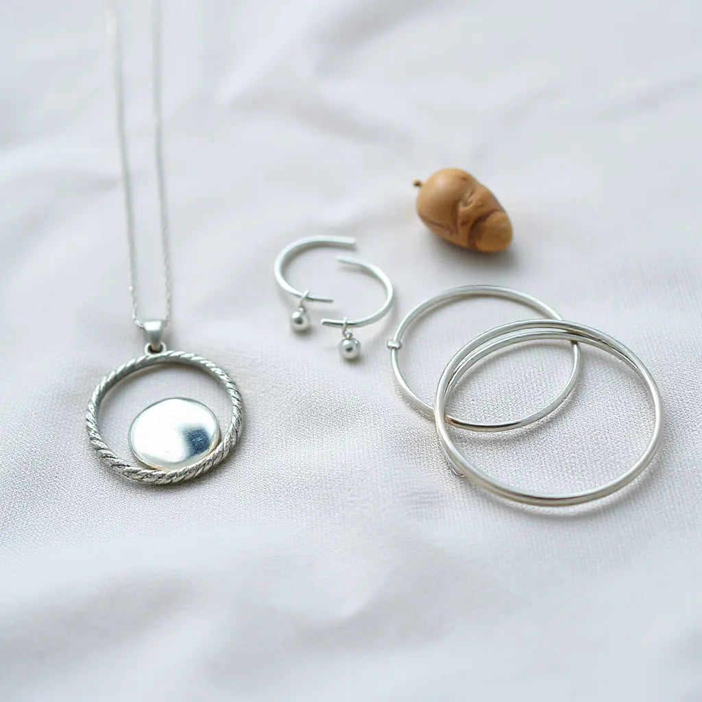 Polished handcrafted silver pendant, earrings, and bangles arranged on neutral fabric under soft natural light